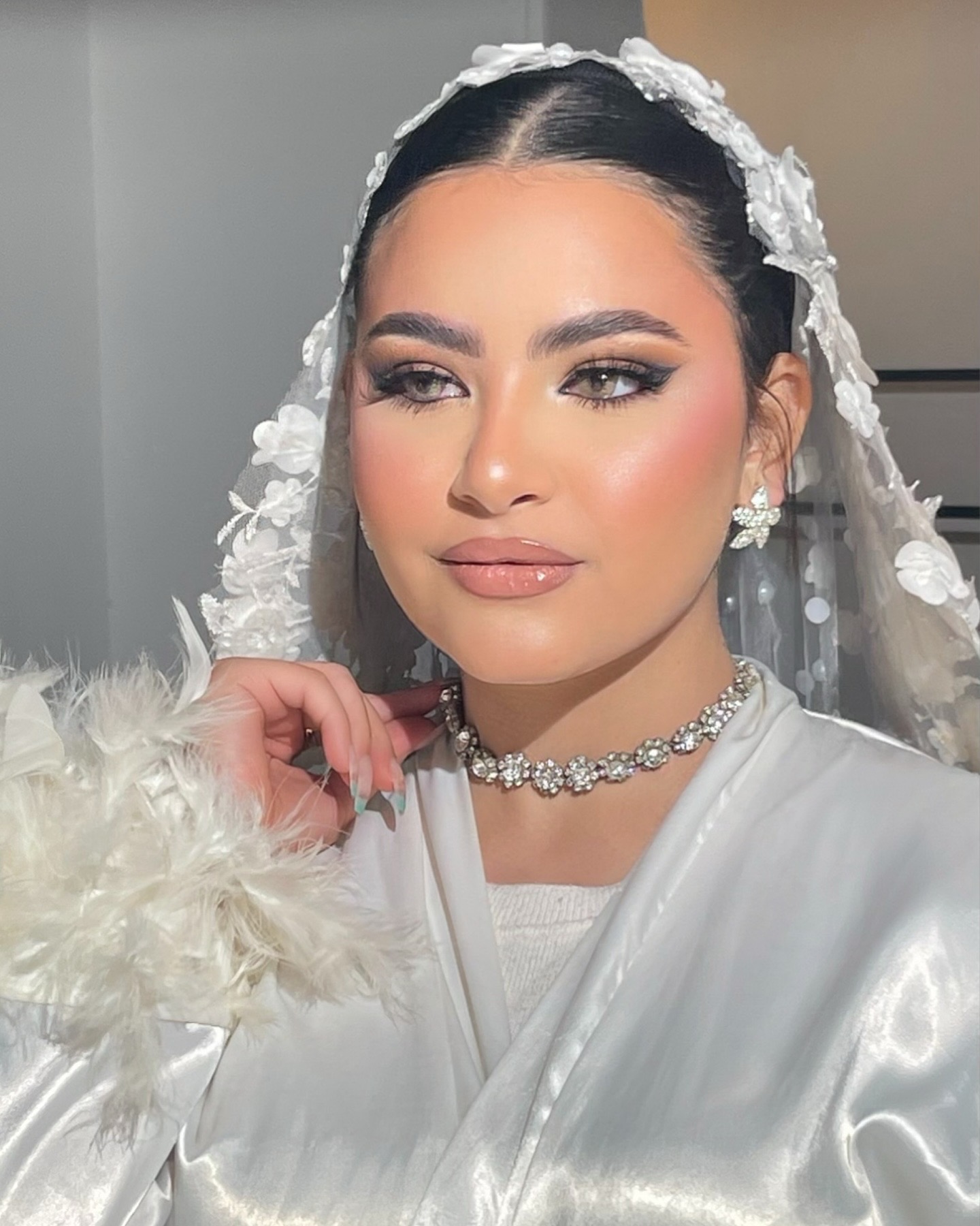 Bride in white satin robe with diamond choker and flower veil